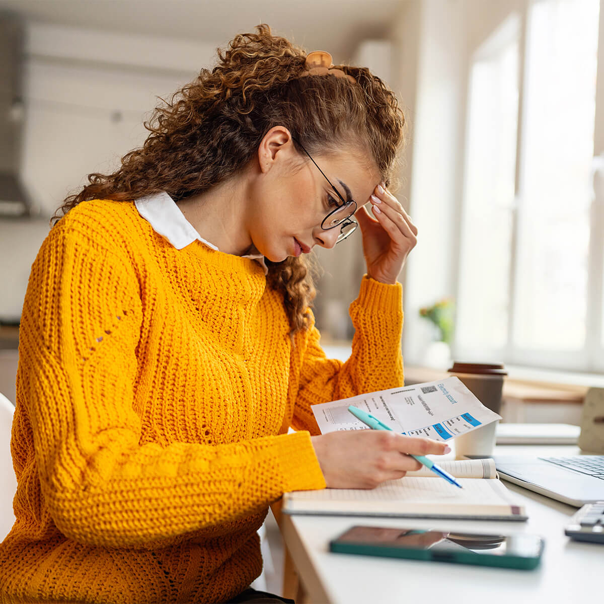 Une femme se tient la tête entre les mains en regardant ses factures