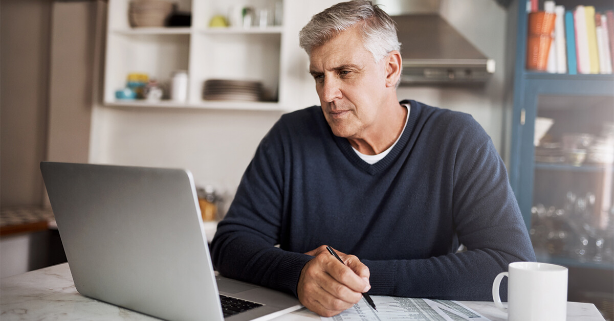 Un homme utilise un ordinateur et un stylo pour calculer son ratio dette/revenu