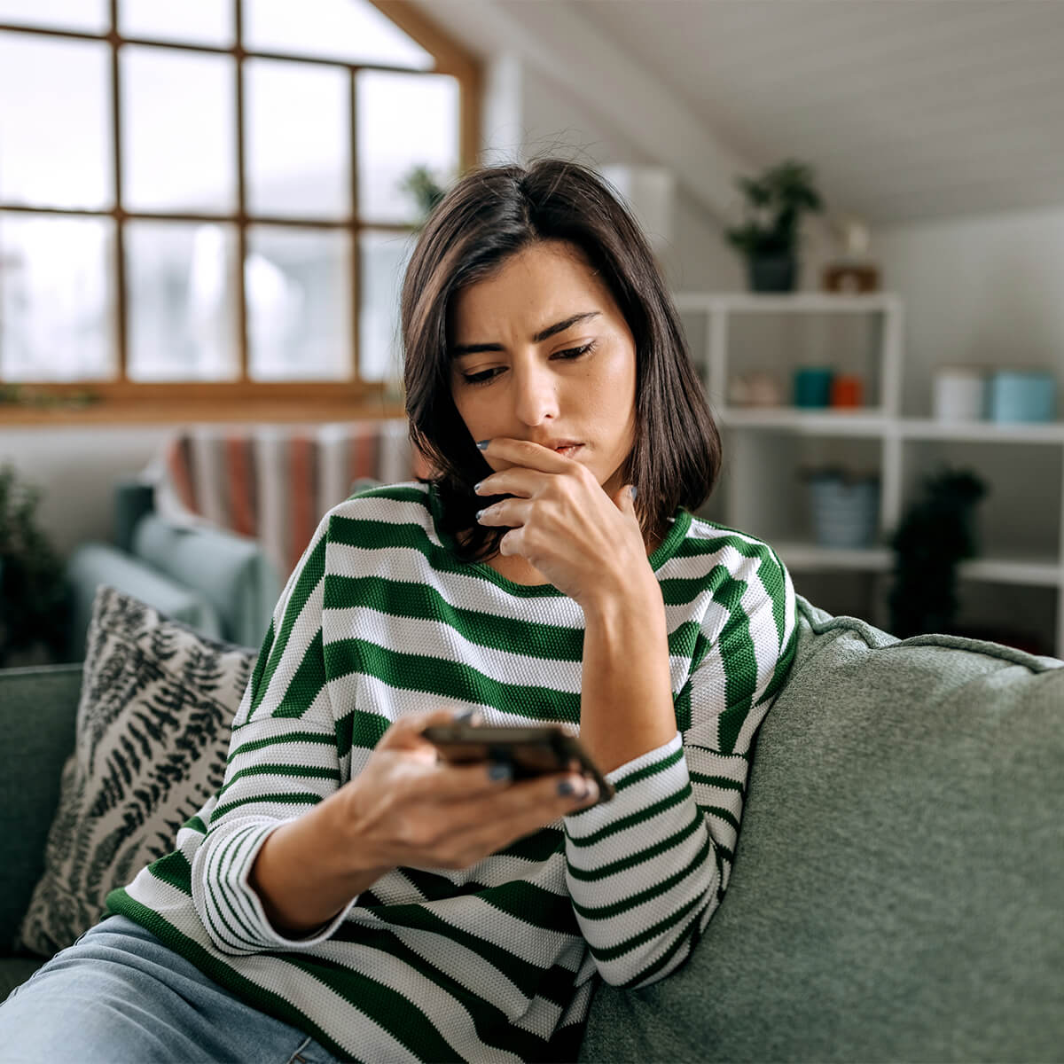 Jeune femme inquiète utilisant un smartphone dans un salon - photo de stock