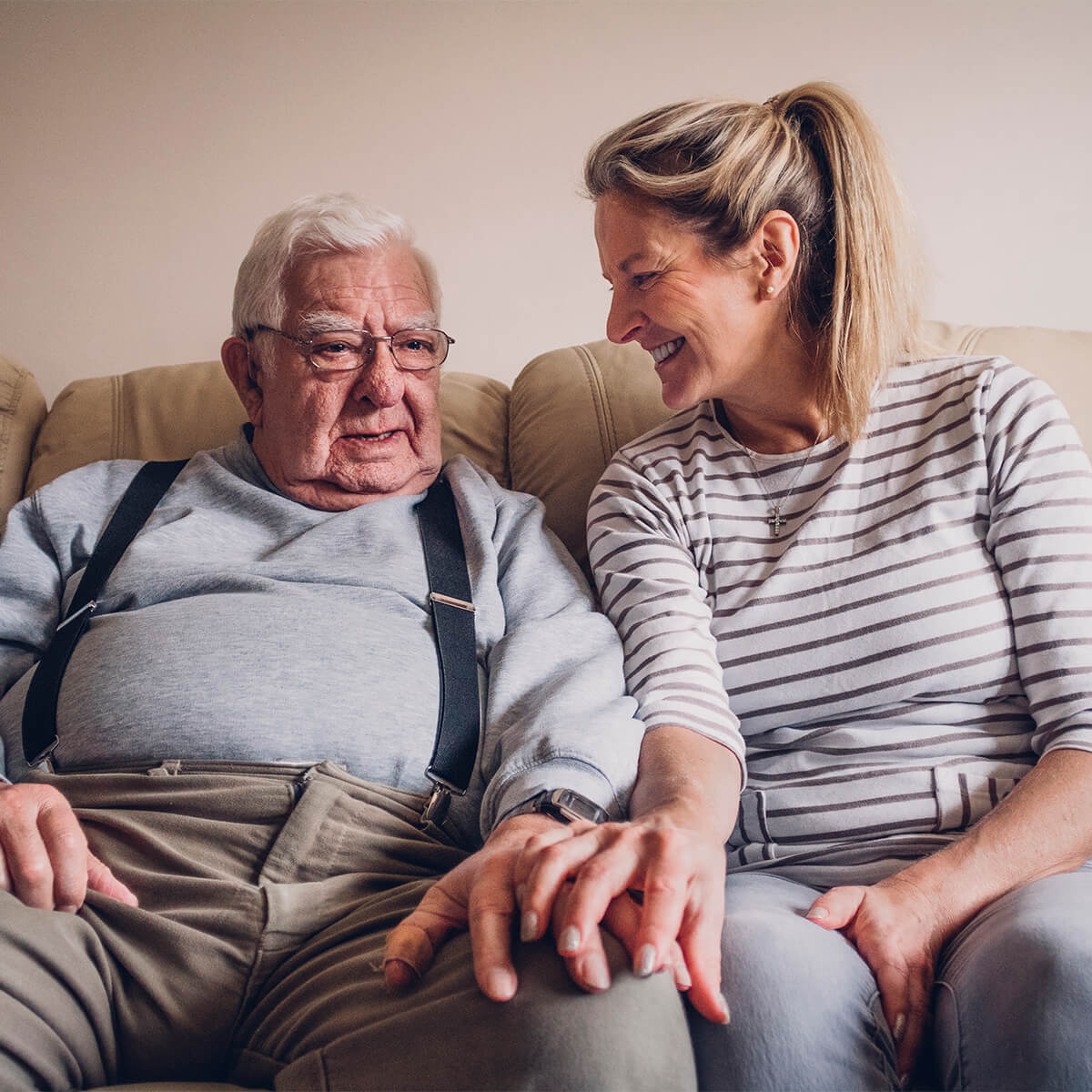 Un homme âgé est assis sur le canapé de son salon à côté de sa fille.