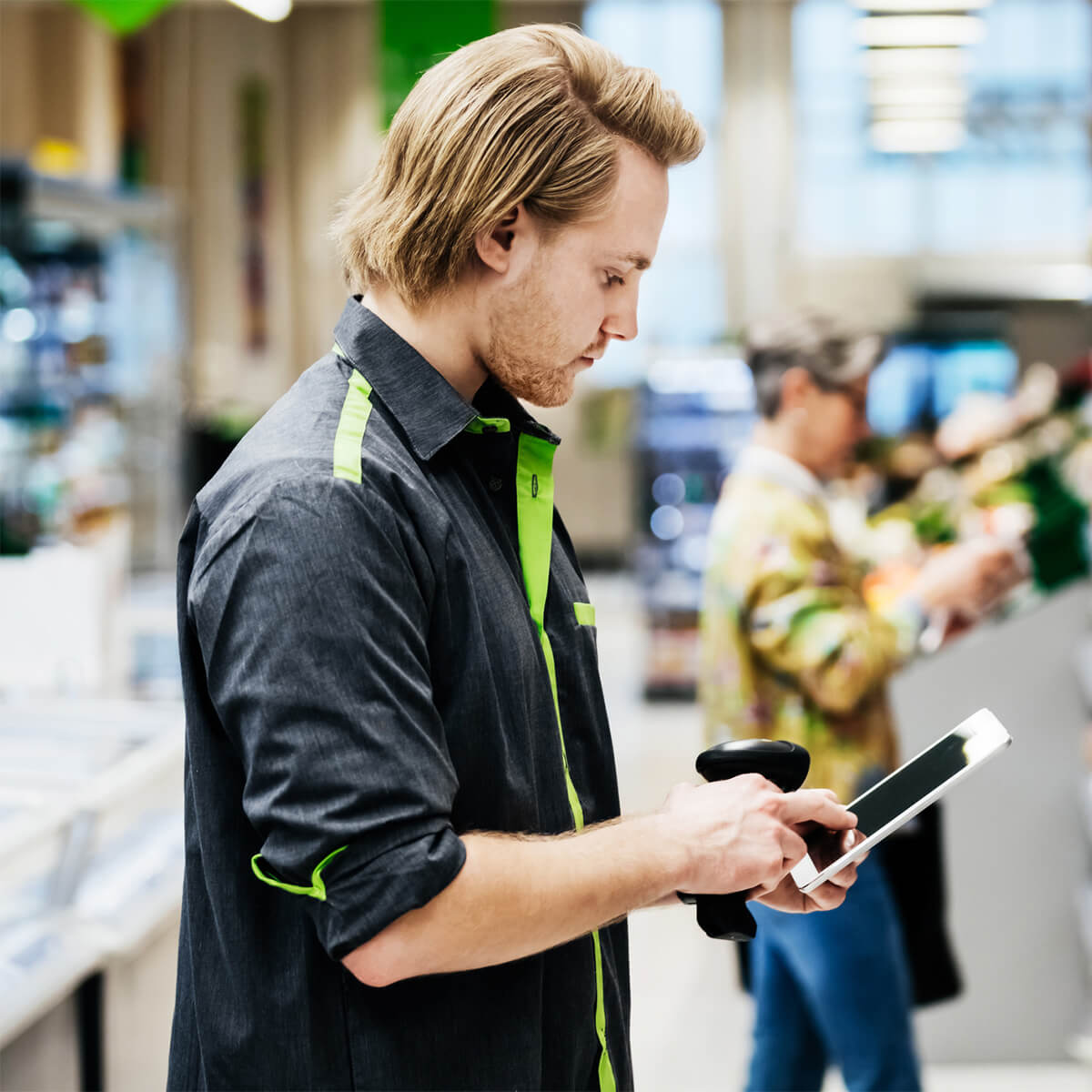 A supermarket employee performing a stock check using a bar code reader and a digital tablet.