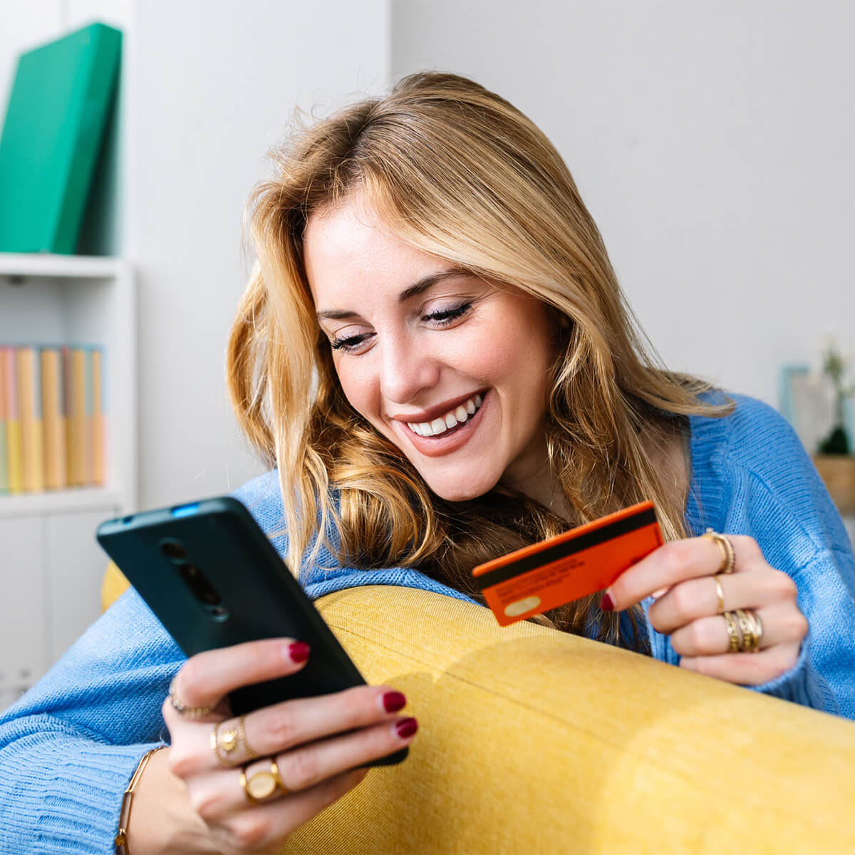 Happy young woman holding credit card while shopping online at home - stock photo