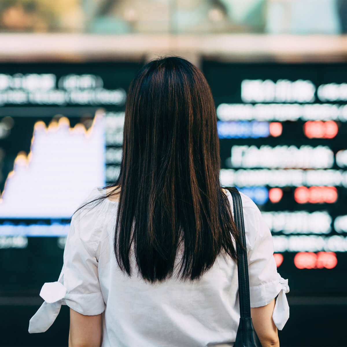 Woman standing in front of stock market listings and worrying about her debt and a recession