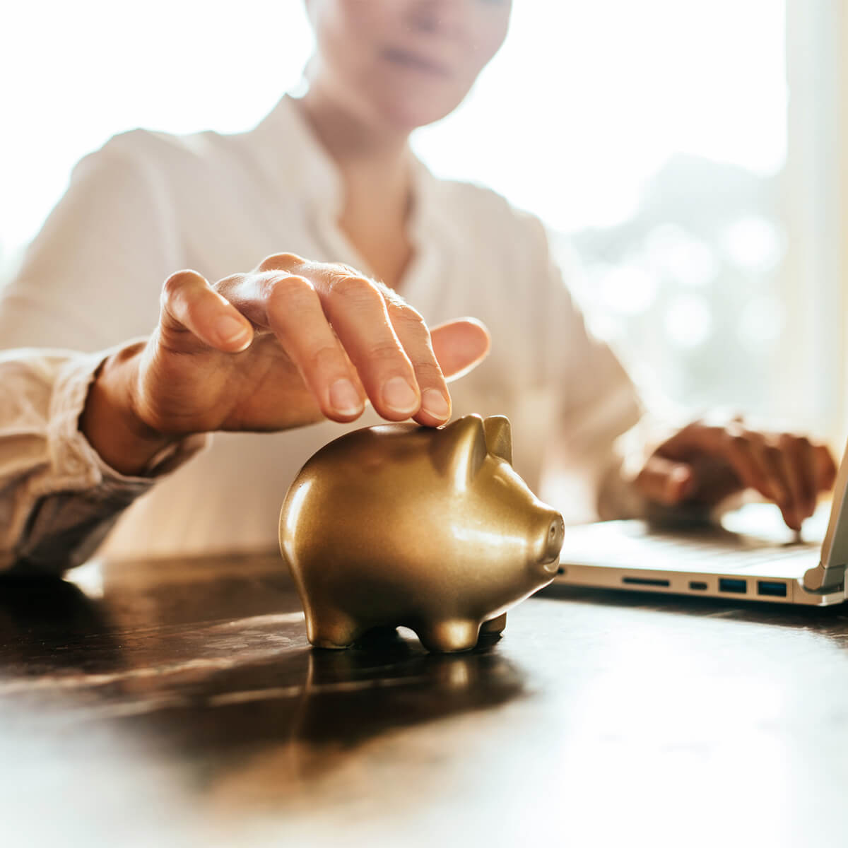 Une femme touche une tirelire dorée devant un ordinateur portable tout en faisant des plans financiers.