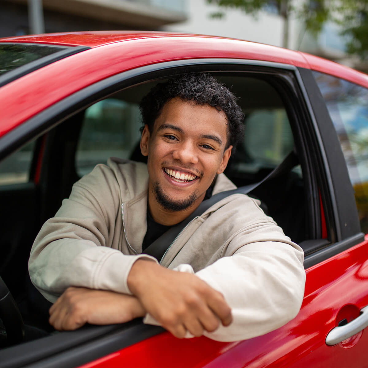 Jeune homme souriant dans une voiture rouge penché par la fenêtre