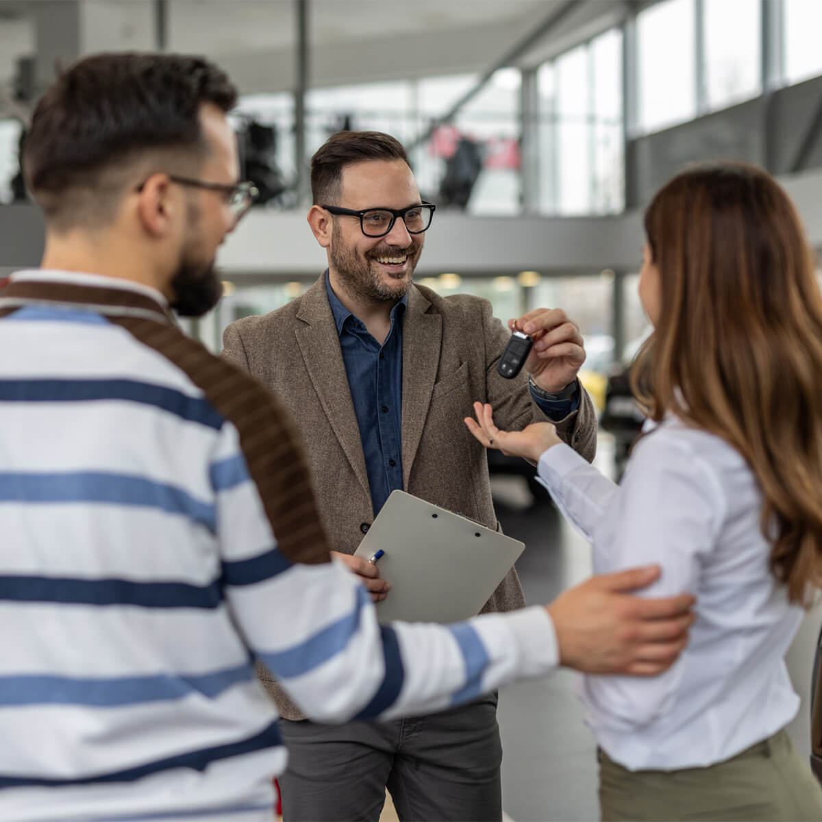Happy car salesman giving keys to a couple in a dealership - stock photo