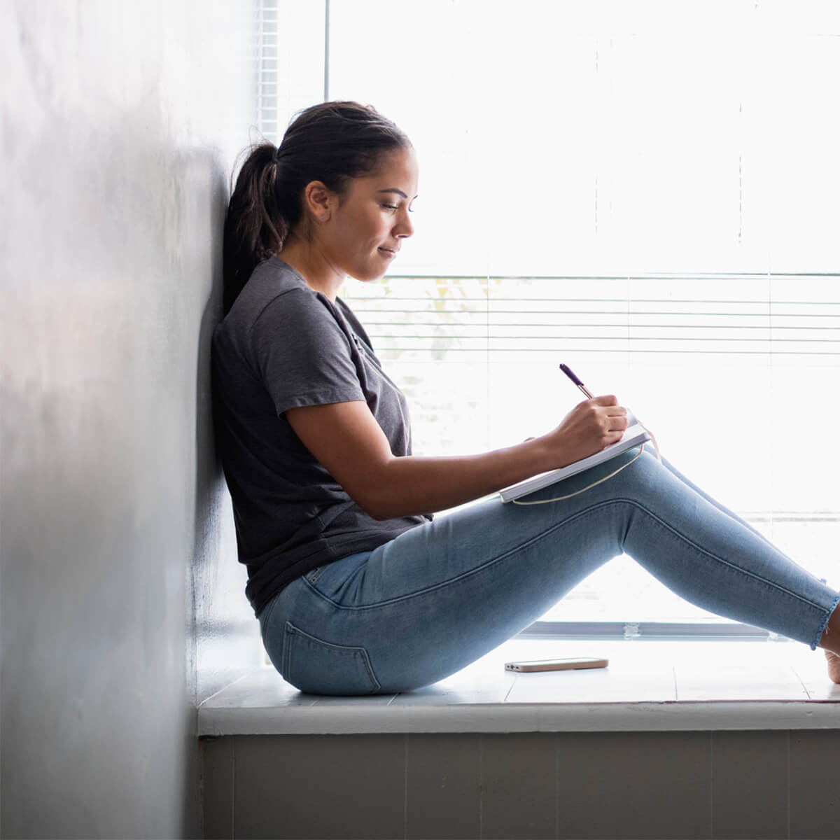 Woman sitting in window seat writing in notebook