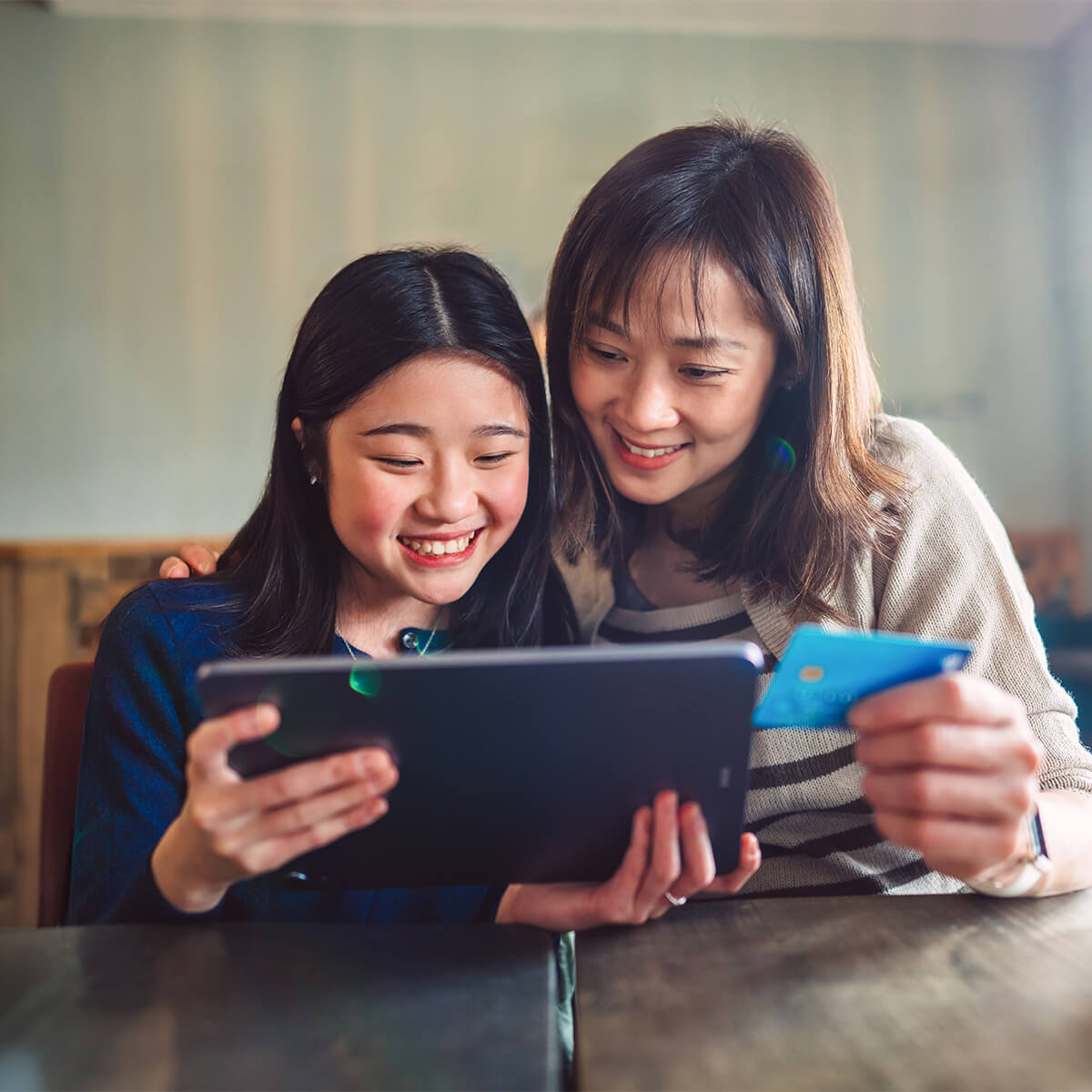 Maman et fille asiatiques joyeuses faisant leurs achats en ligne avec carte de crédit sur tablette numérique tout en profitant de la pause-café dans un café.