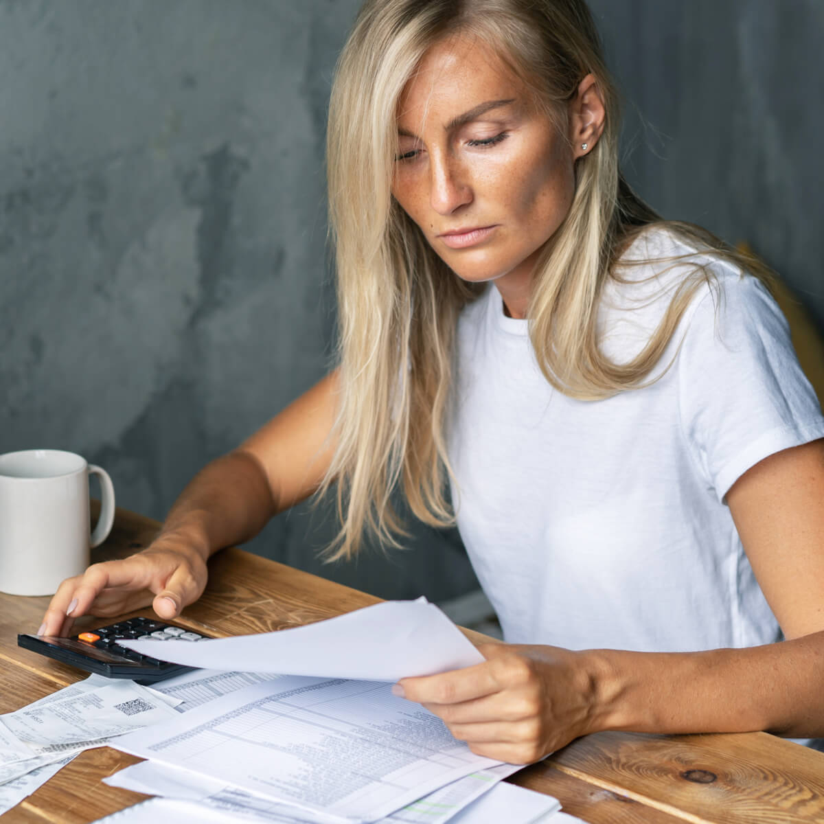 A woman looks at bills on a table while using a calculator