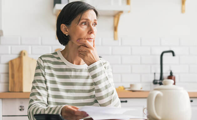 Woman pondering personal finances at home. Sitting at a table with documents and a calculator in front of her.